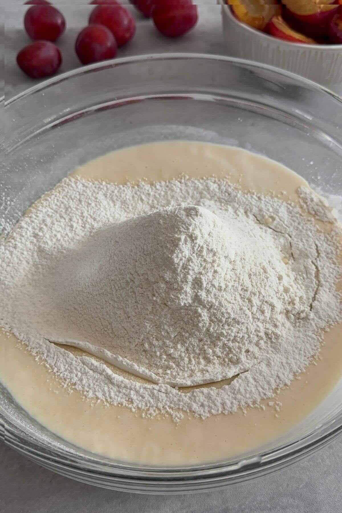 Sifted flour, baking powder, and baking soda added to the pale, fluffy egg-sugar mixture for kefir plum cake.