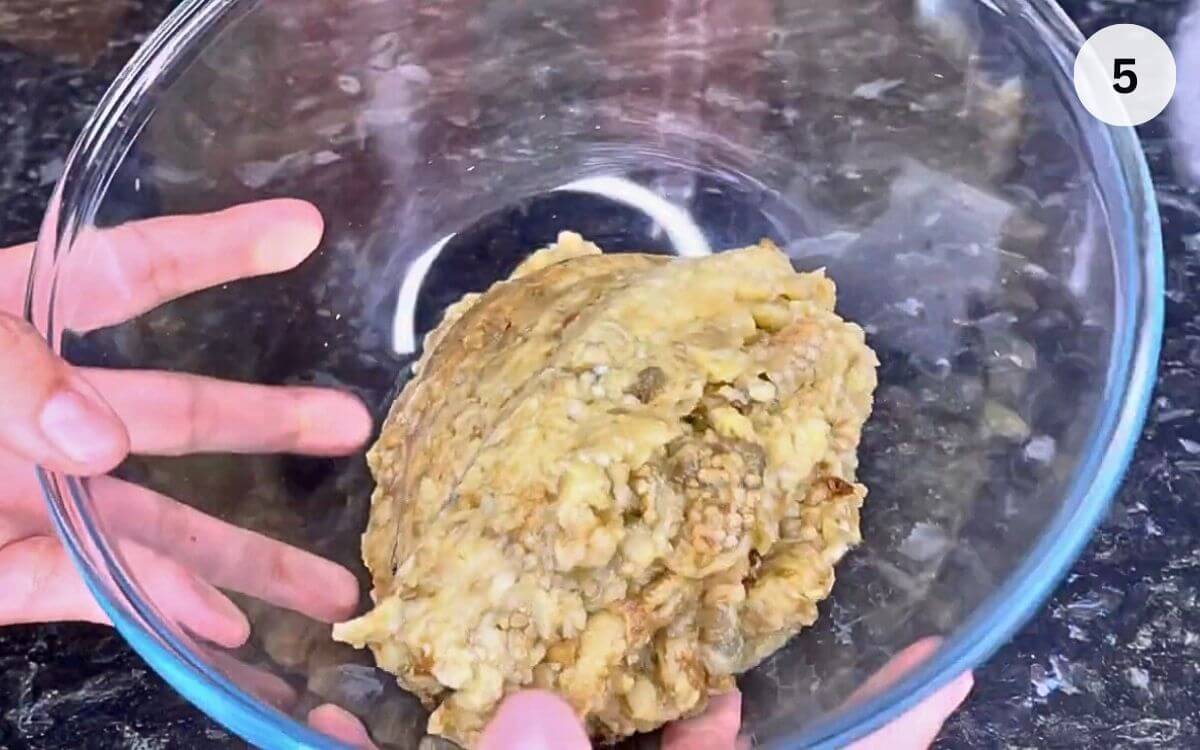Drained eggplant being mashed in a glass bowl.