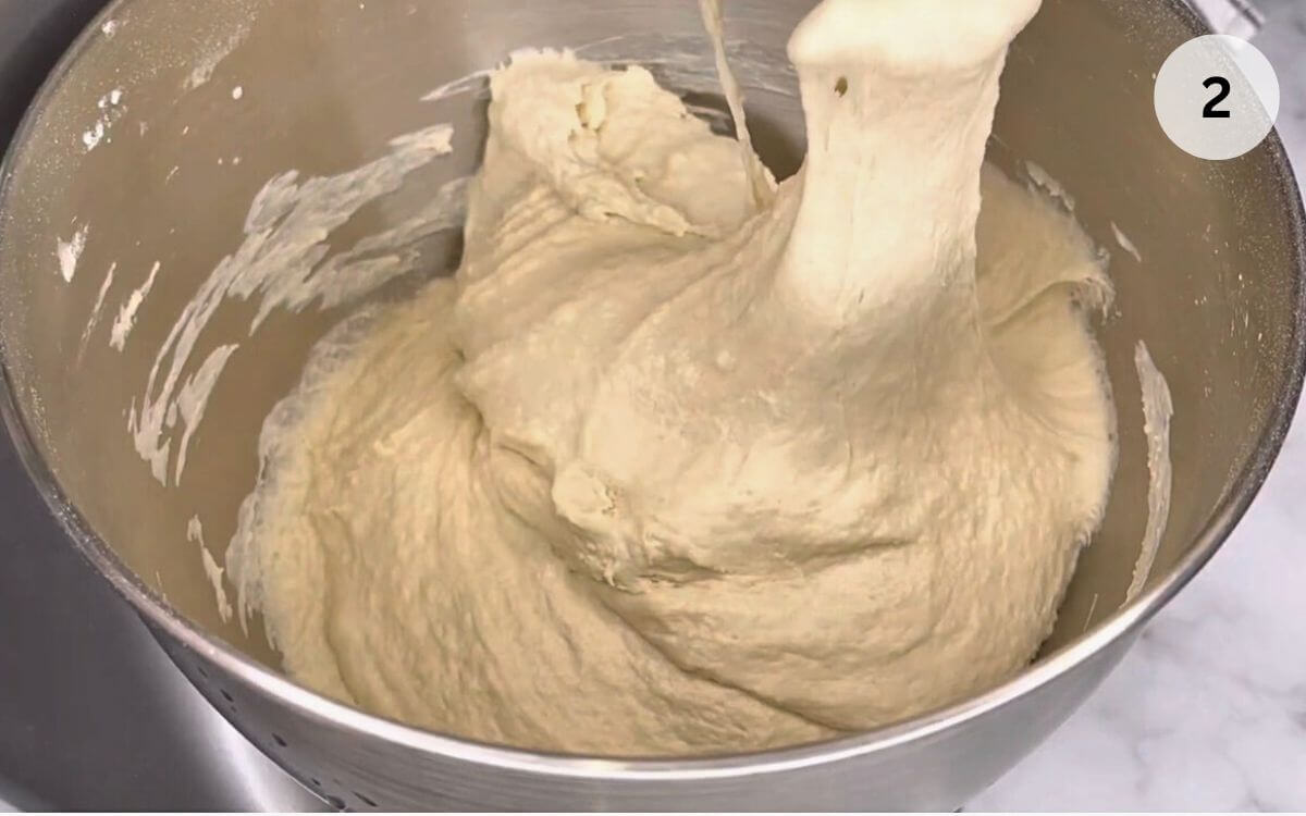 Adding remaining flour and salt, kneading the Romanian bread dough by hand for a smooth texture.
