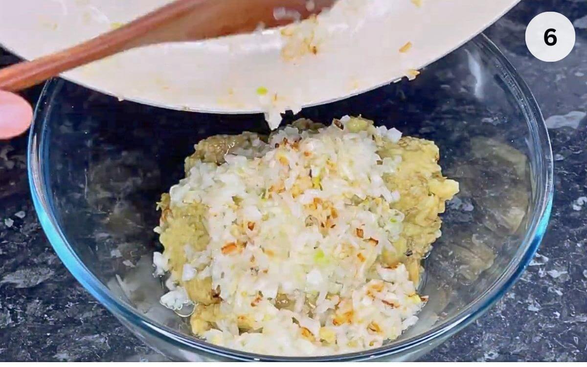 Golden-brown sautéed onions being added to mashed eggplant in a bowl.