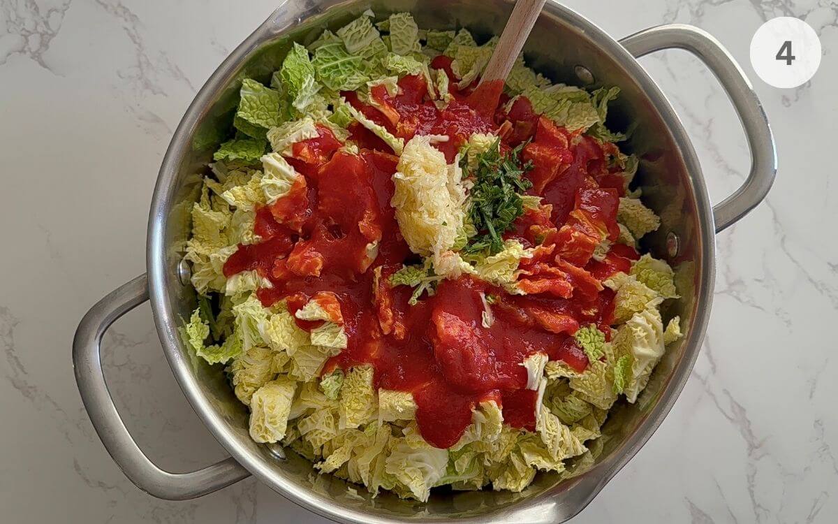 Adding tomato juice and herbs over seasoned cabbage in a cooking pot.