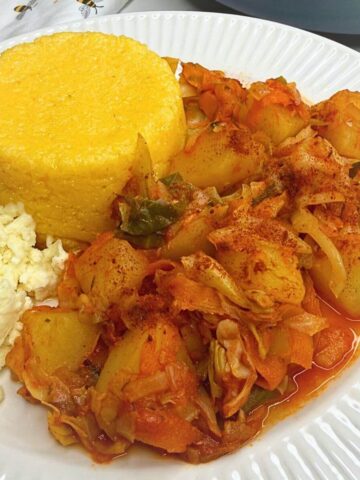 A plate of finished Romanian cabbage potato stew with polenta and cheese.