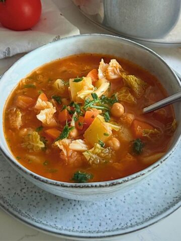A steaming bowl of hearty cabbage potato soup with carrots and chickpeas.