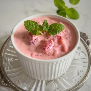 A close up of a ceramic white dish filled with a creamy pink strawberry dessert garnishes with mint leaves.
