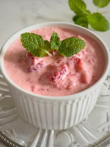 A close up of a ceramic white dish filled with a creamy pink strawberry dessert garnishes with mint leaves.