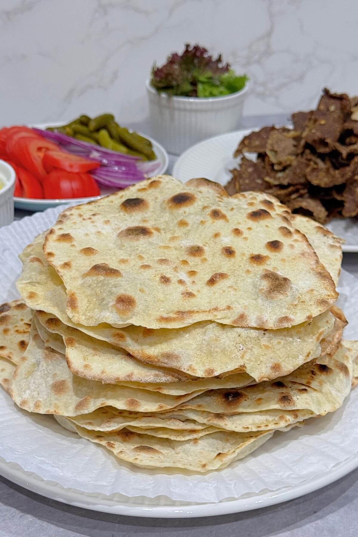 Stack of warm, pliable soft flour tortillas showing the golden brown cooking spots.