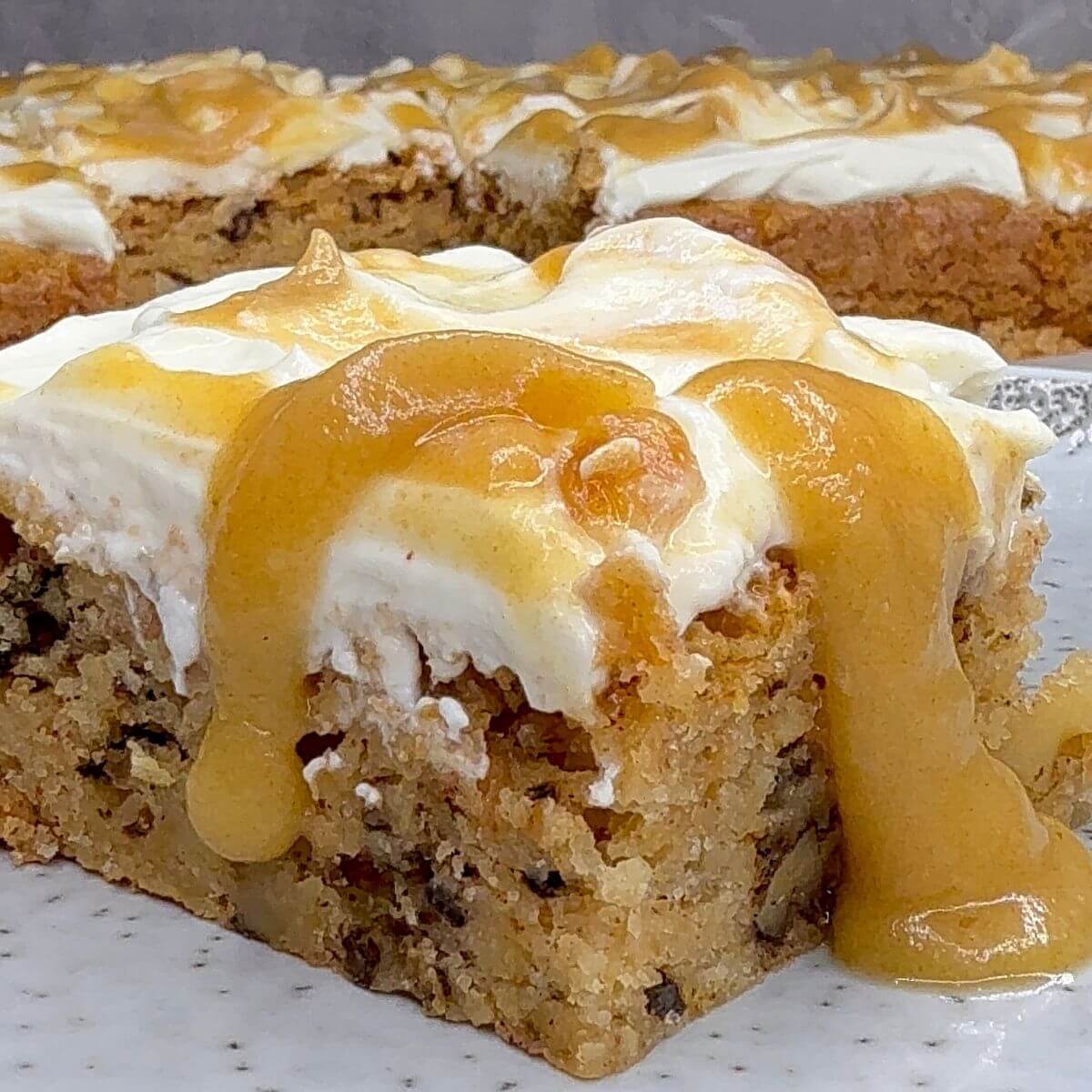 A slice of moist apple cake with swirled yogurt cream cheese frosting and caramel drizzle.