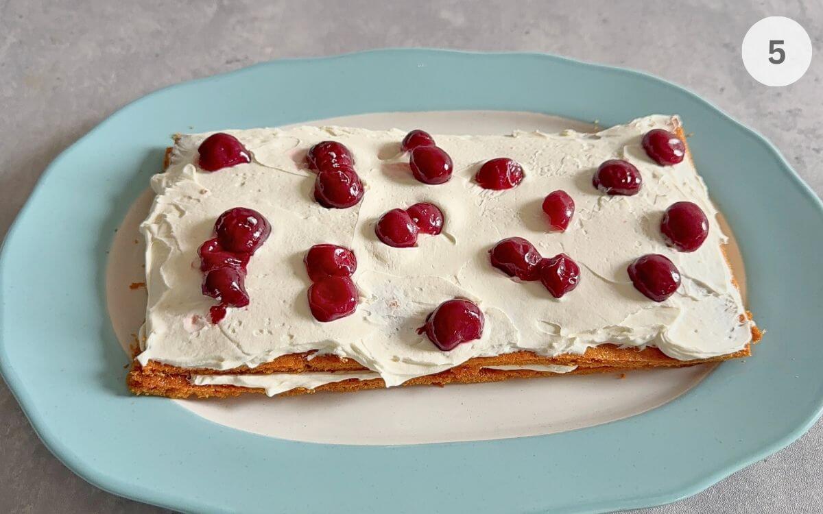 A layer of honey cake topped with white cream and several dark red sour cherries.