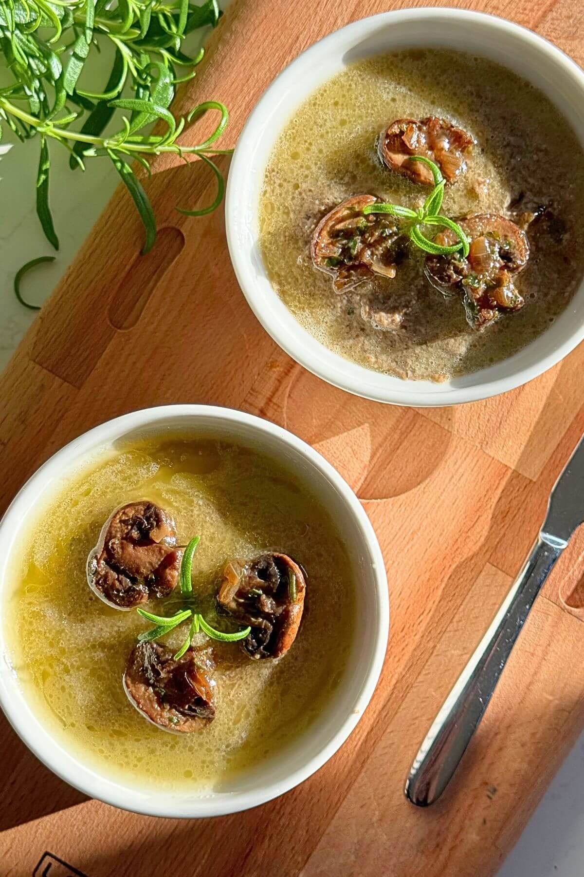 Homemade mushroom paté in two serving dishes, topped with mushrooms and rosemary.