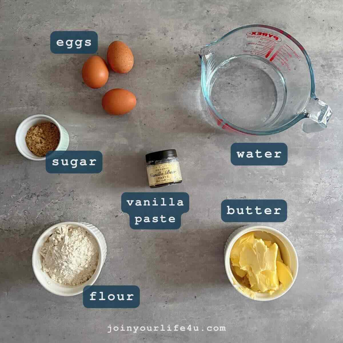 Eggs, butter, flour, sugar, water, vanilla, individually displayed on a table.