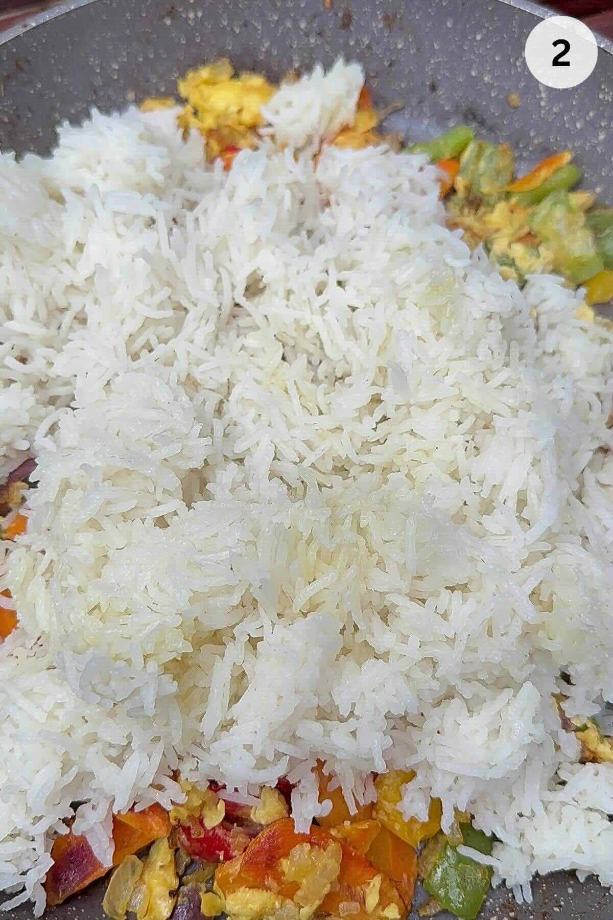 Adding cold cooked rice to vegetable fried rice in wok breaking up clumps.