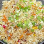 Healthy fried rice with frozen vegetables in a wok with scrambled eggs and green onions.