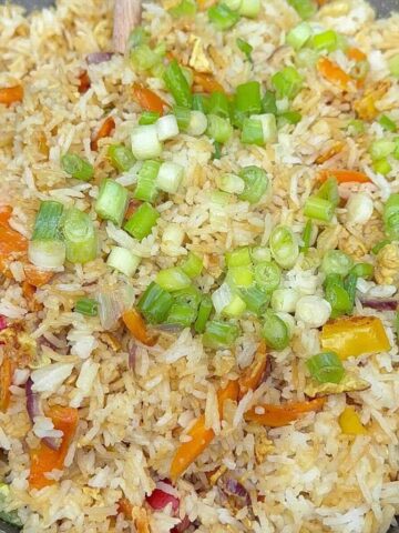 Healthy fried rice with frozen vegetables in a wok with scrambled eggs and green onions.