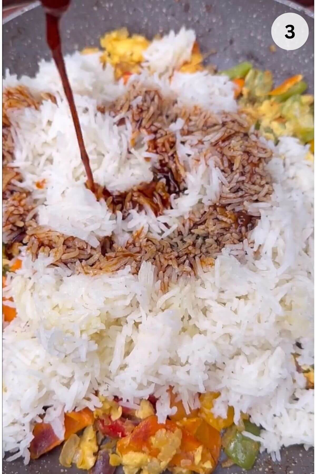 Pouring soy sauce and oyster sauce mixture over fried rice in wok.