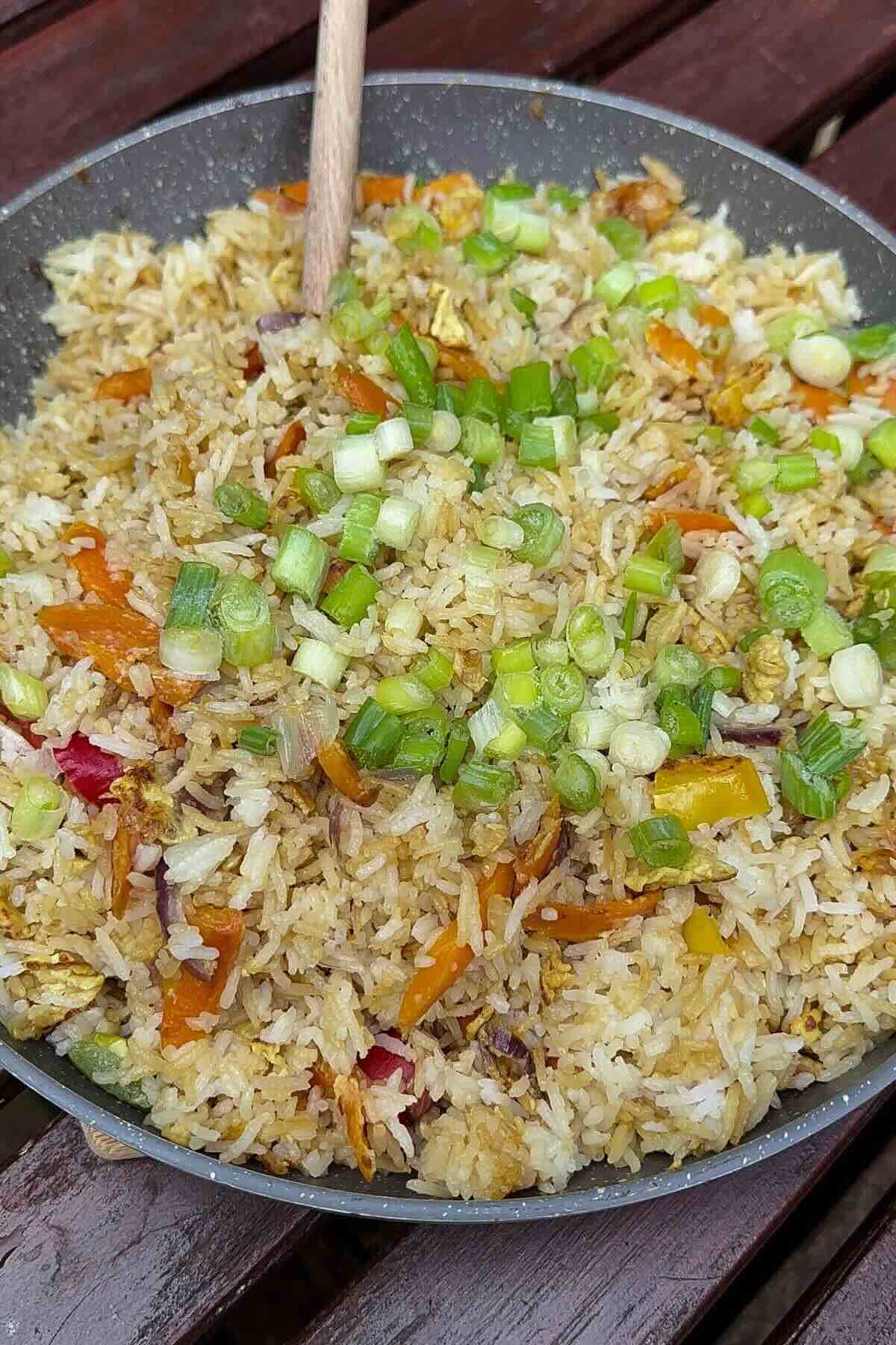 Healthy fried rice with frozen vegetables in a wok with scrambled eggs and green onions.