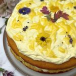 Three Layer Lemon Cake decorated with lemon cream cheese frosting, lemon curd swirls and edible flowers.