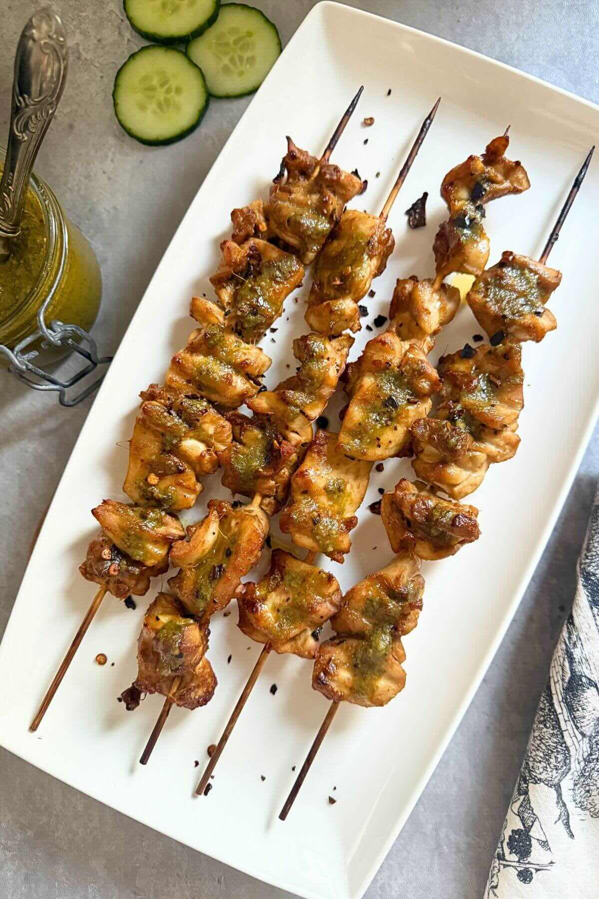 Grilled chicken satay skewers drizzled with green Thai basil pesto sauce on a white platter