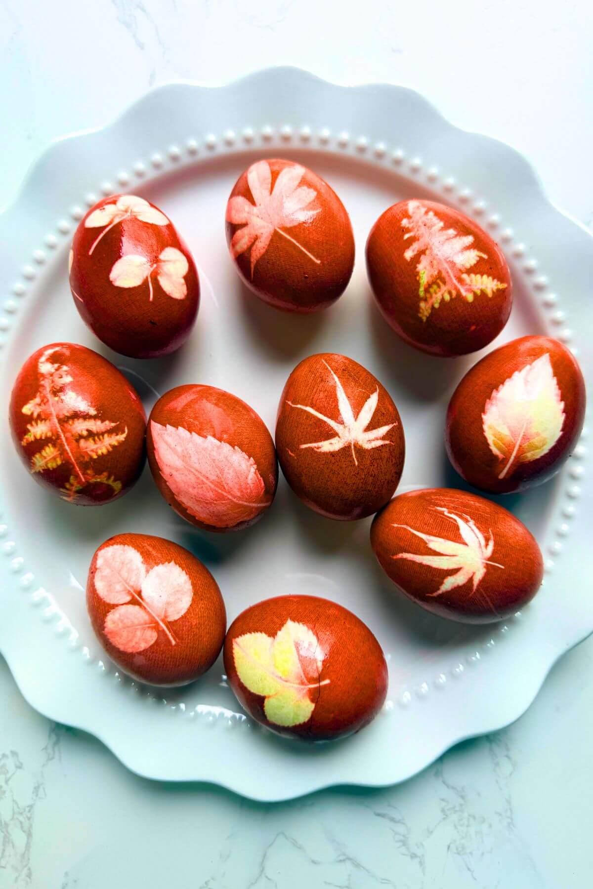Romanian naturally dyed Easter eggs with leaf prints on white plate, deep burgundy red tones.