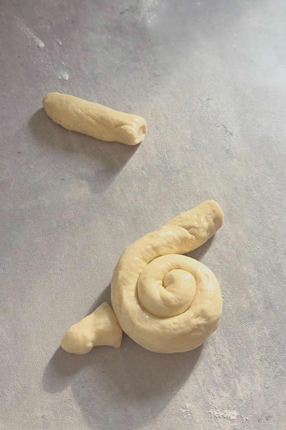 Dough coiled into bunny body with small dough ball attached as tail.