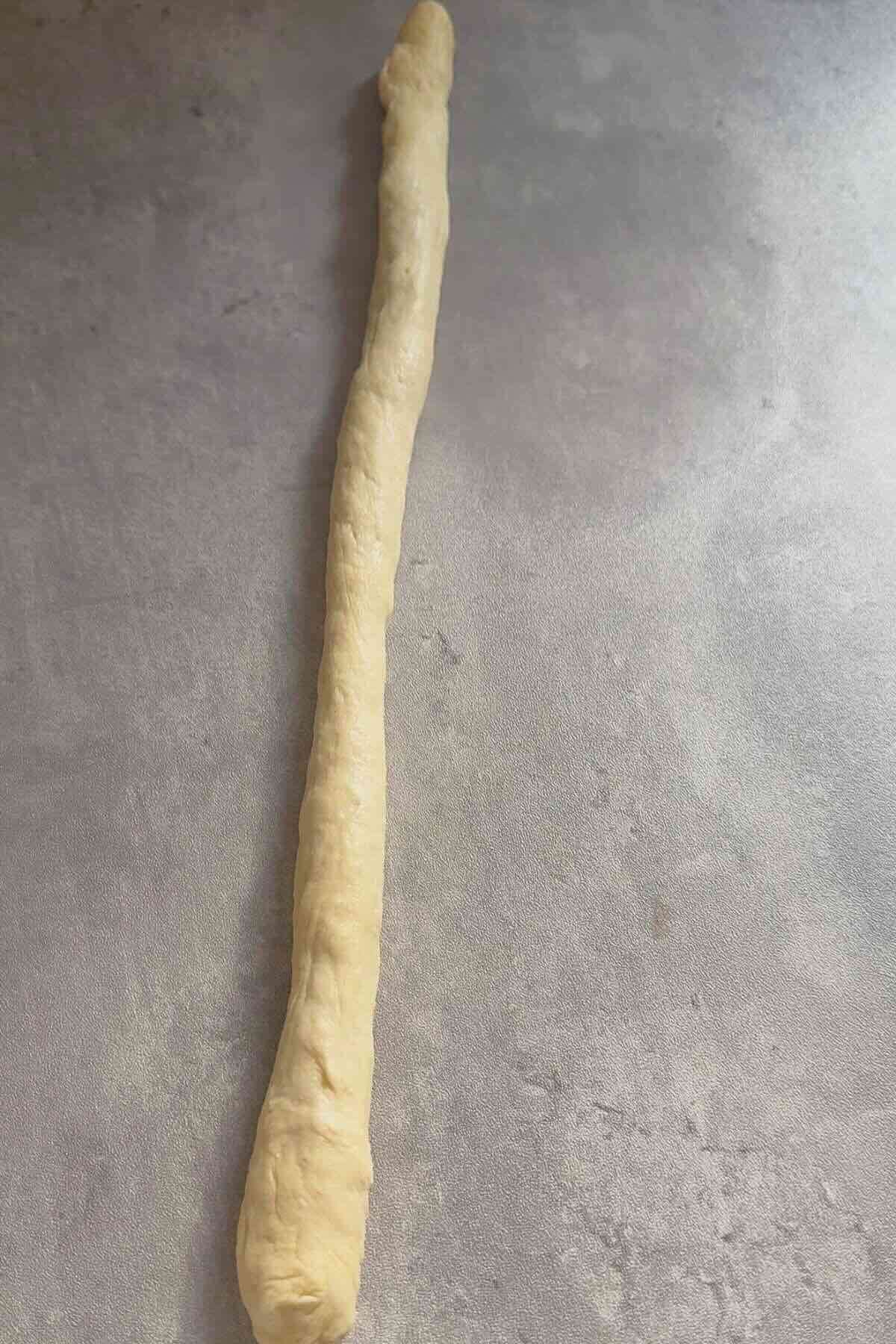 Dough rolled into a long rope on a clean work surface.