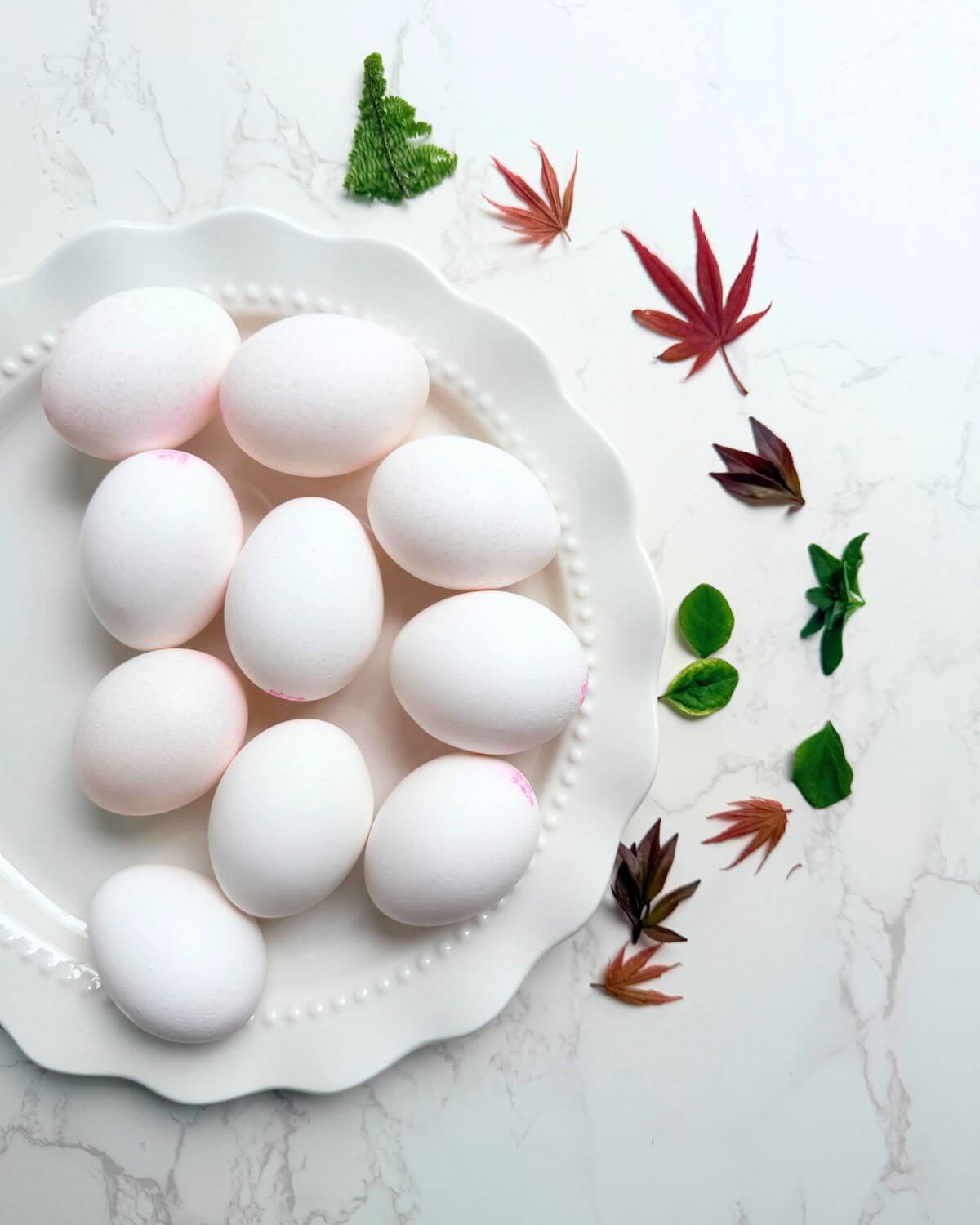 Washed and dried white eggs on a clean surface with fresh leaves laid out beside them ready for wrapping.