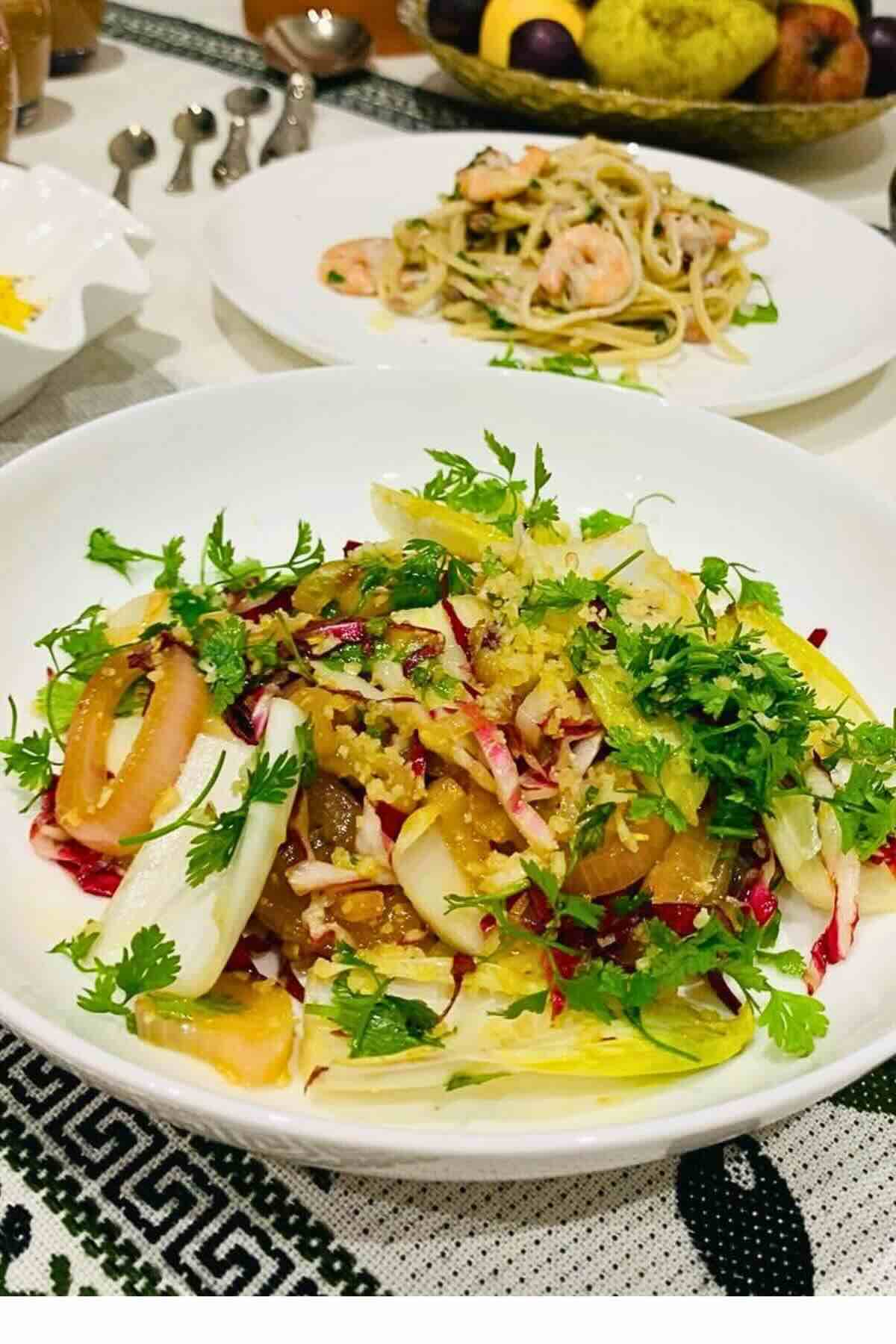 Chicory salad with clementine dressing pomegranate seeds and pine nuts in a white bowl.