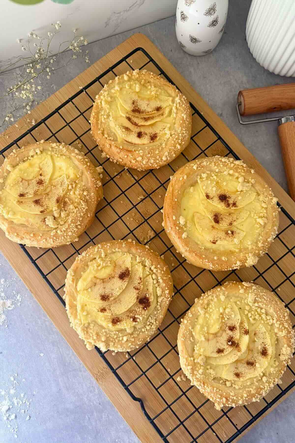 Golden apple custard crumble buns on a tray dusted with powdered sugar.