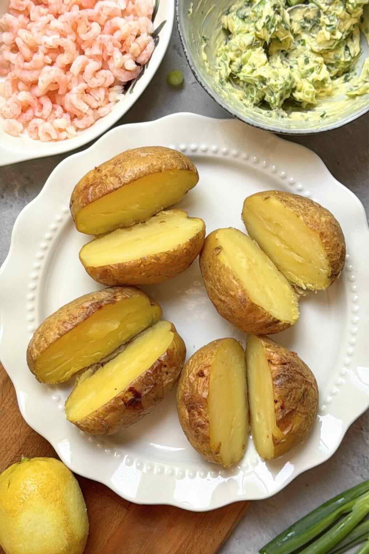 Baked potatoes split in halved ready to be filled with prawns and garlic butter.