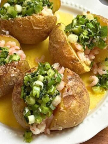 Plated baked potato with shrimp arugula and cherry tomatoes.