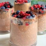 Chocolate berry protein overnight oats served in a glass with fresh mixed berries on top.