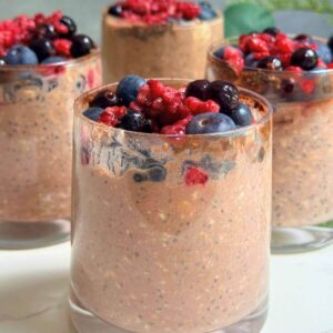 Chocolate berry protein overnight oats served in a glass with fresh mixed berries on top.