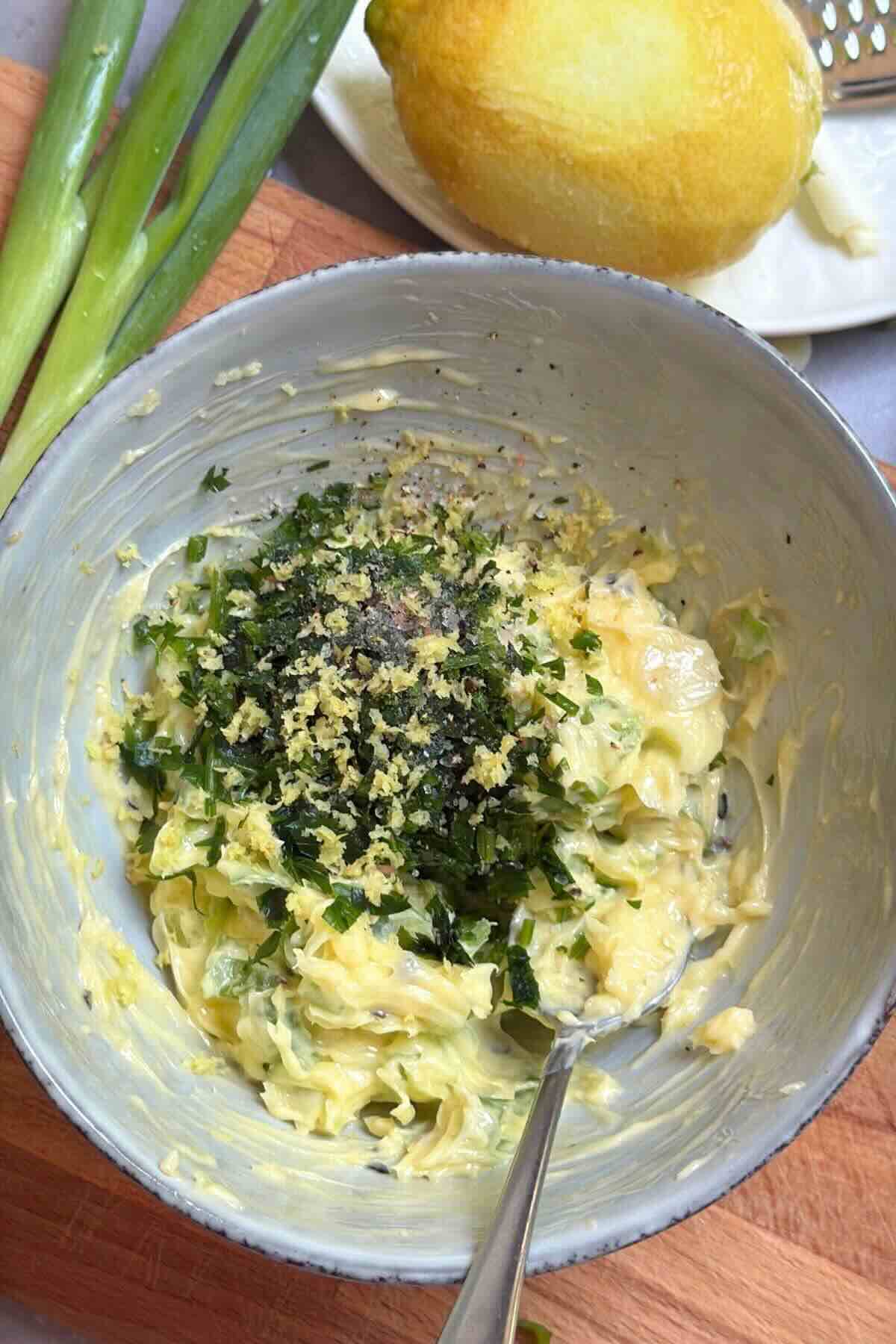 Garlic butter mixed with green onion parsley and lemon zest in bowl.