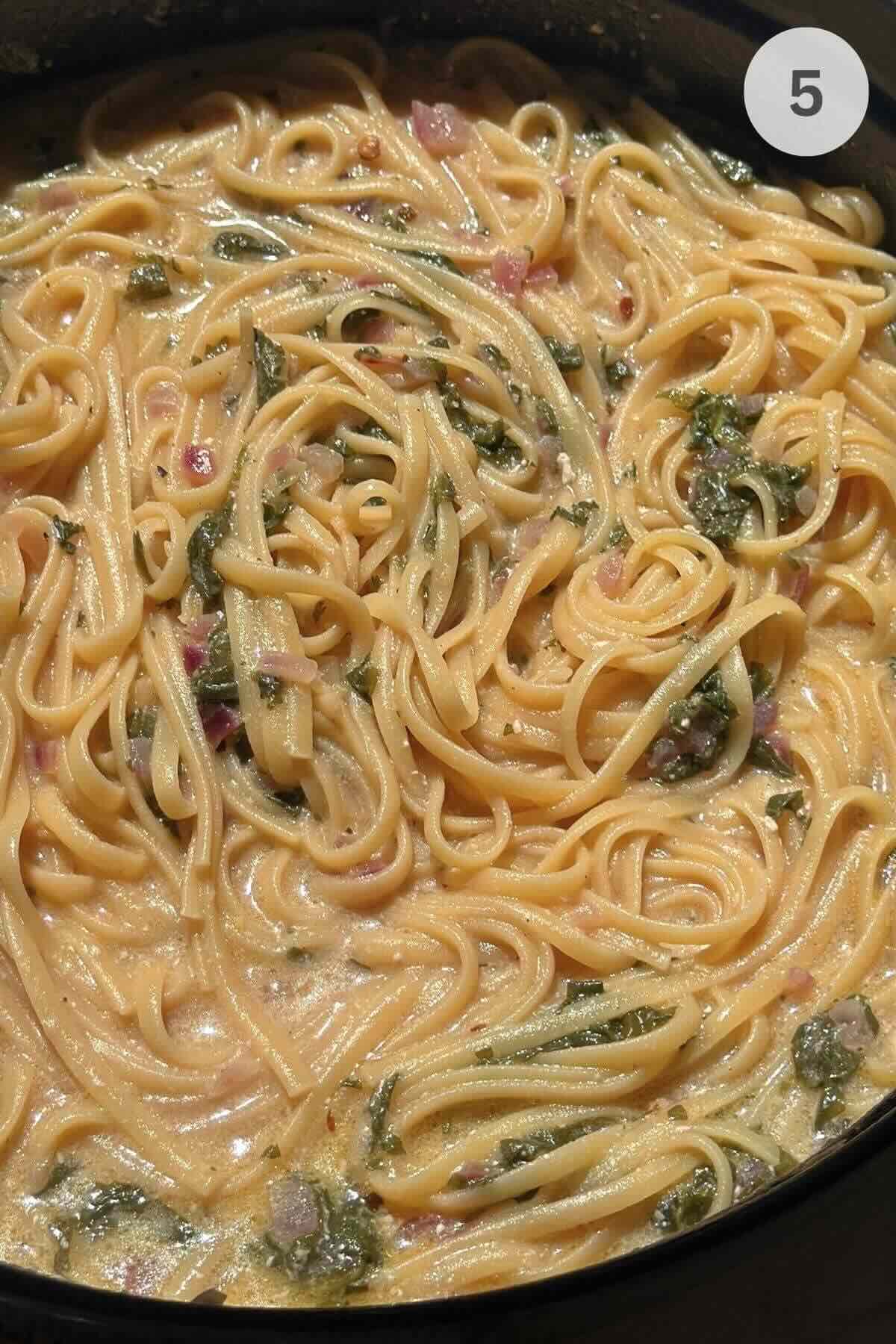 Creamy shrimp linguine pasta cooking in skillet with sauce and spinach.