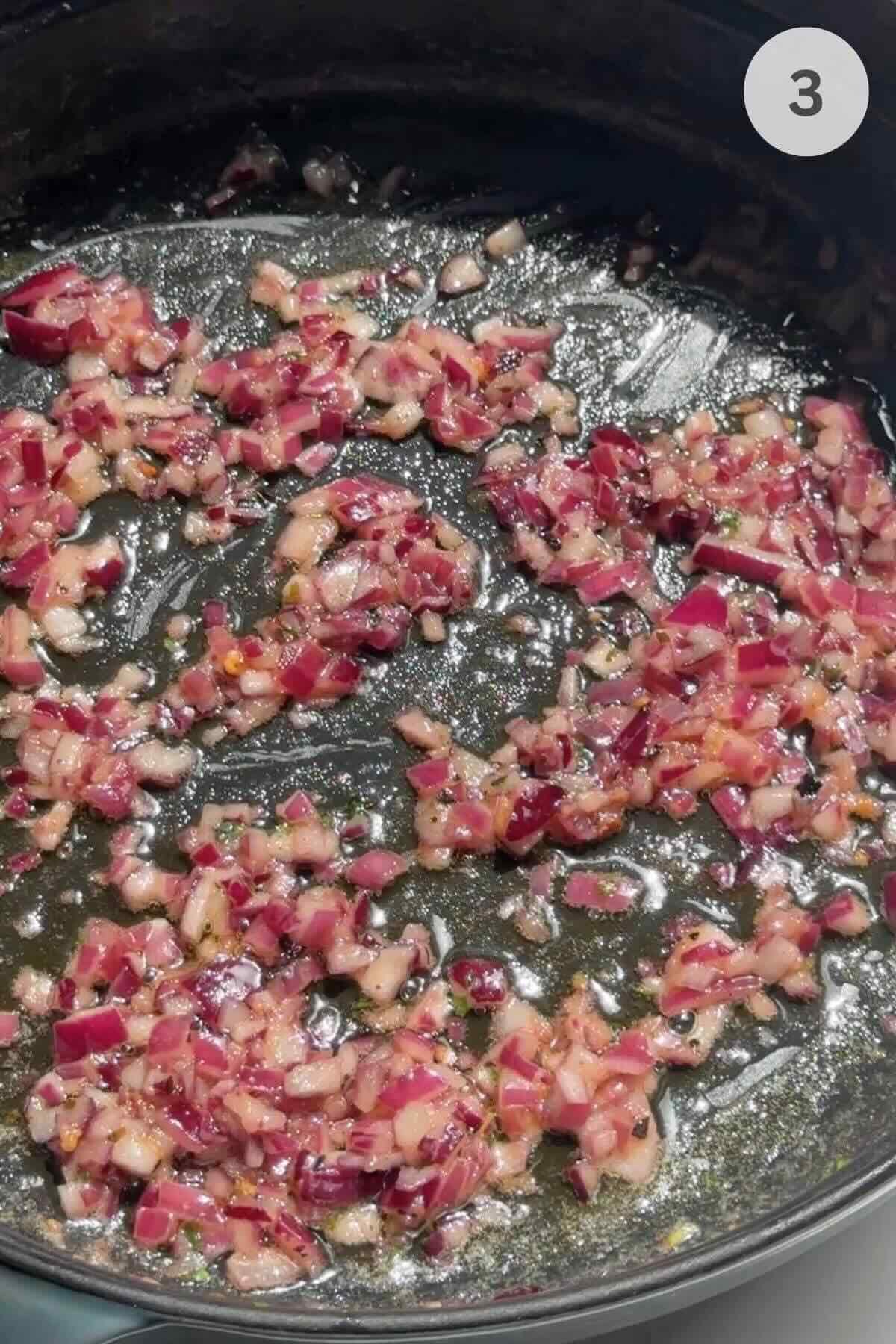 Sautéed onion, red chili, and garlic cooking in a skillet for shrimp linguine.