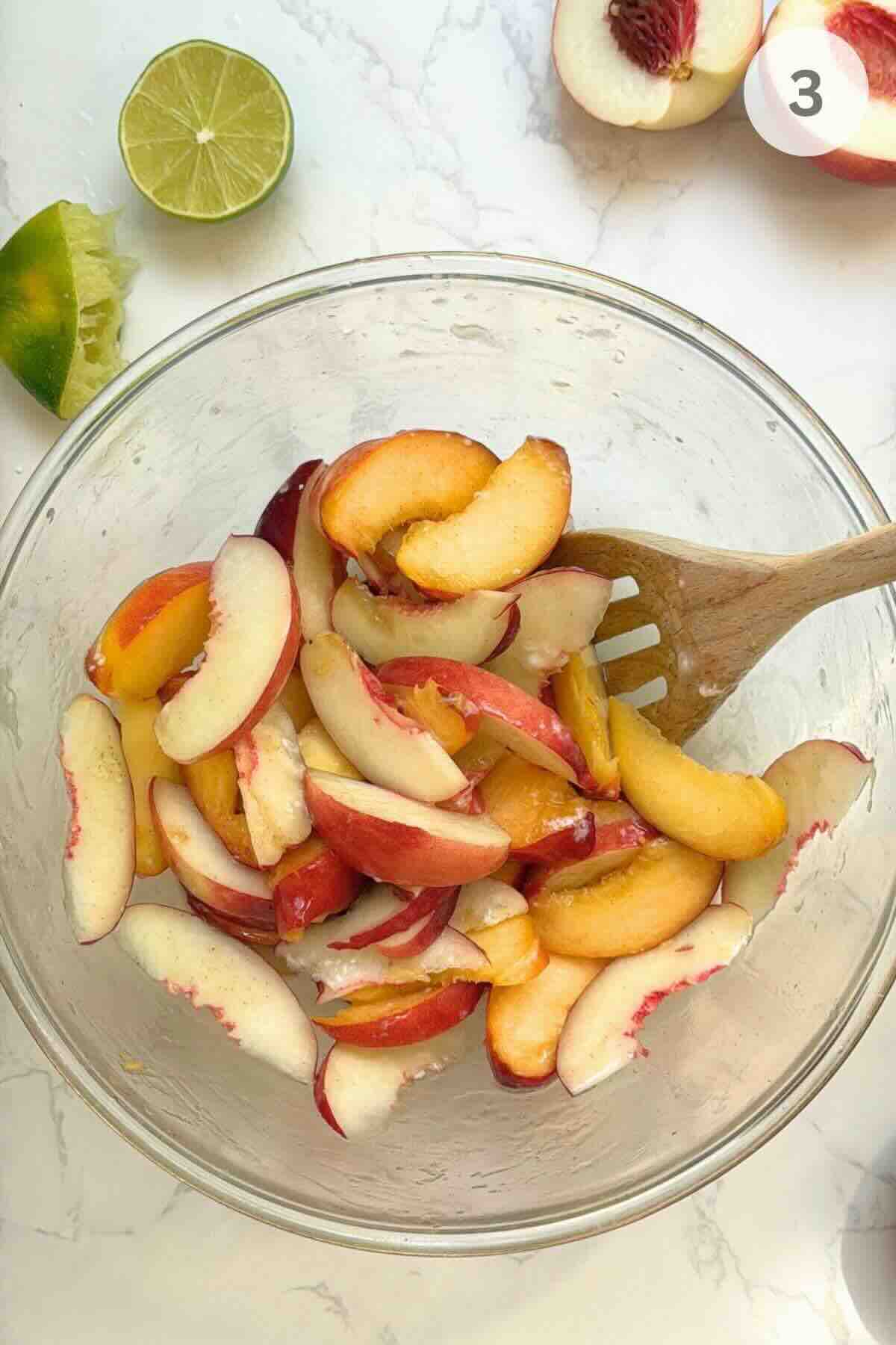 Showing sliced peaches coated evenly with citrus juice, vanilla, and sugar.
