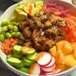 Cooked tuna poke bowl with seared tuna, sushi rice, avocado, and mango in a bowl.