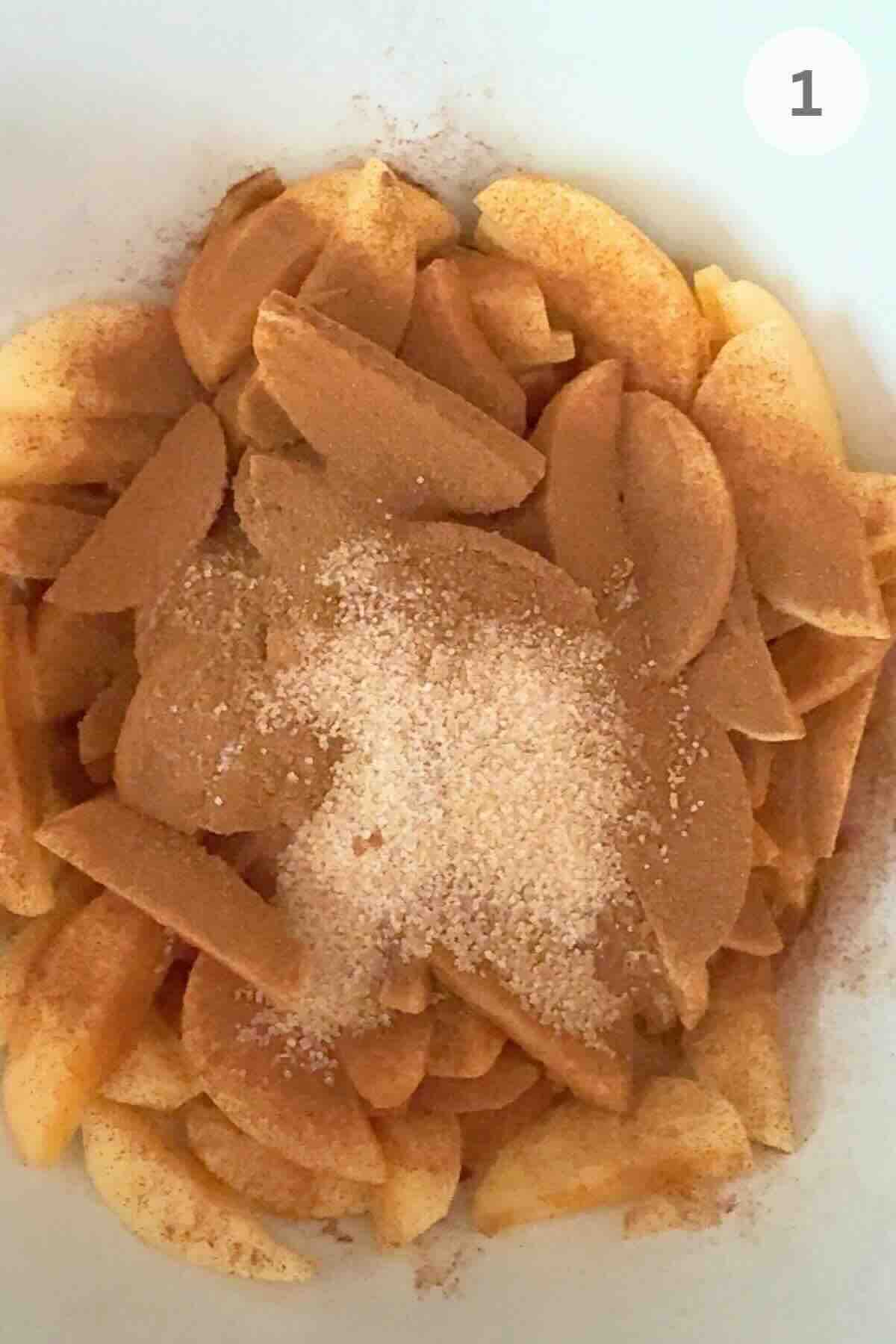Apples tossed with cinnamon and sugar in a mixing bowl.