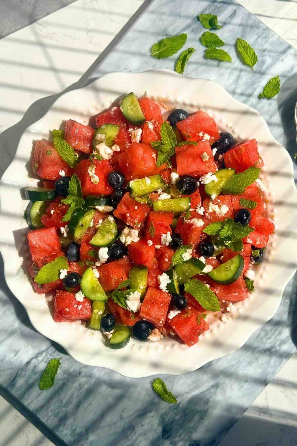 Watermelon cucumber feta salad with mint and lime dressing in a white bowl.