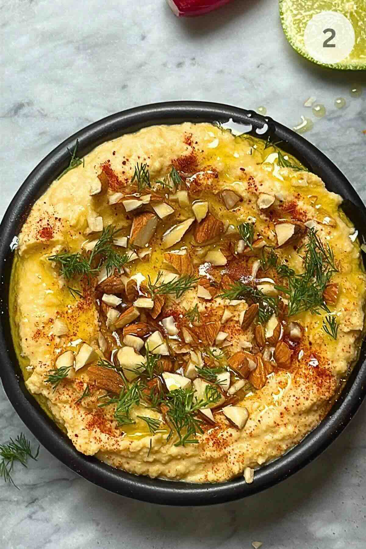 Spooning the smooth chickpea dip into a bowl and drizzling it with olive oil.