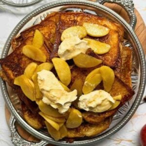 Golden brioche French toast topped with maple caramelized apples and a spoonful of whipped cream.