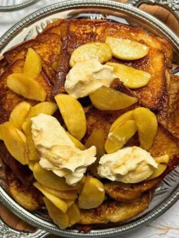 Golden brioche French toast topped with maple caramelized apples and a spoonful of whipped cream.