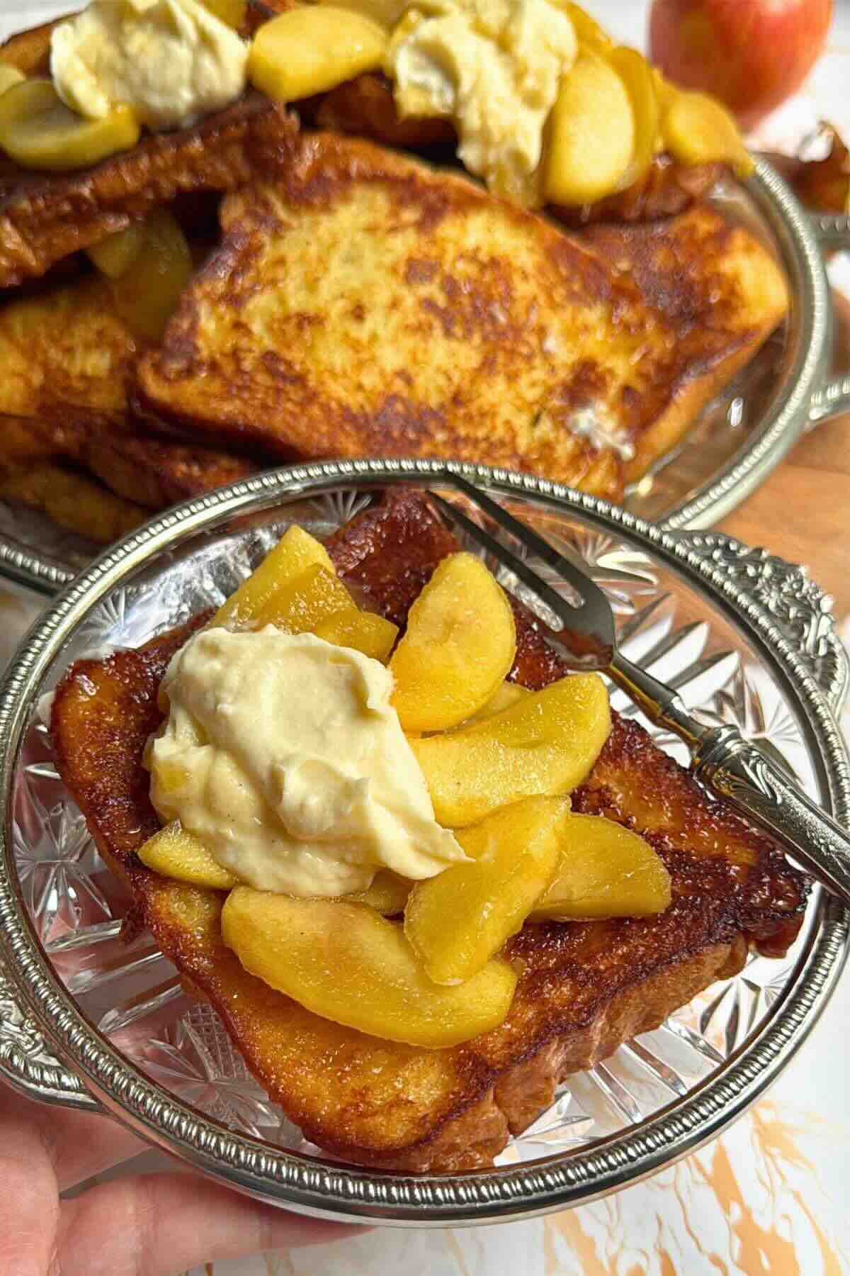 Golden brioche French toast topped with maple caramelized apples and a spoonful of whipped cream.