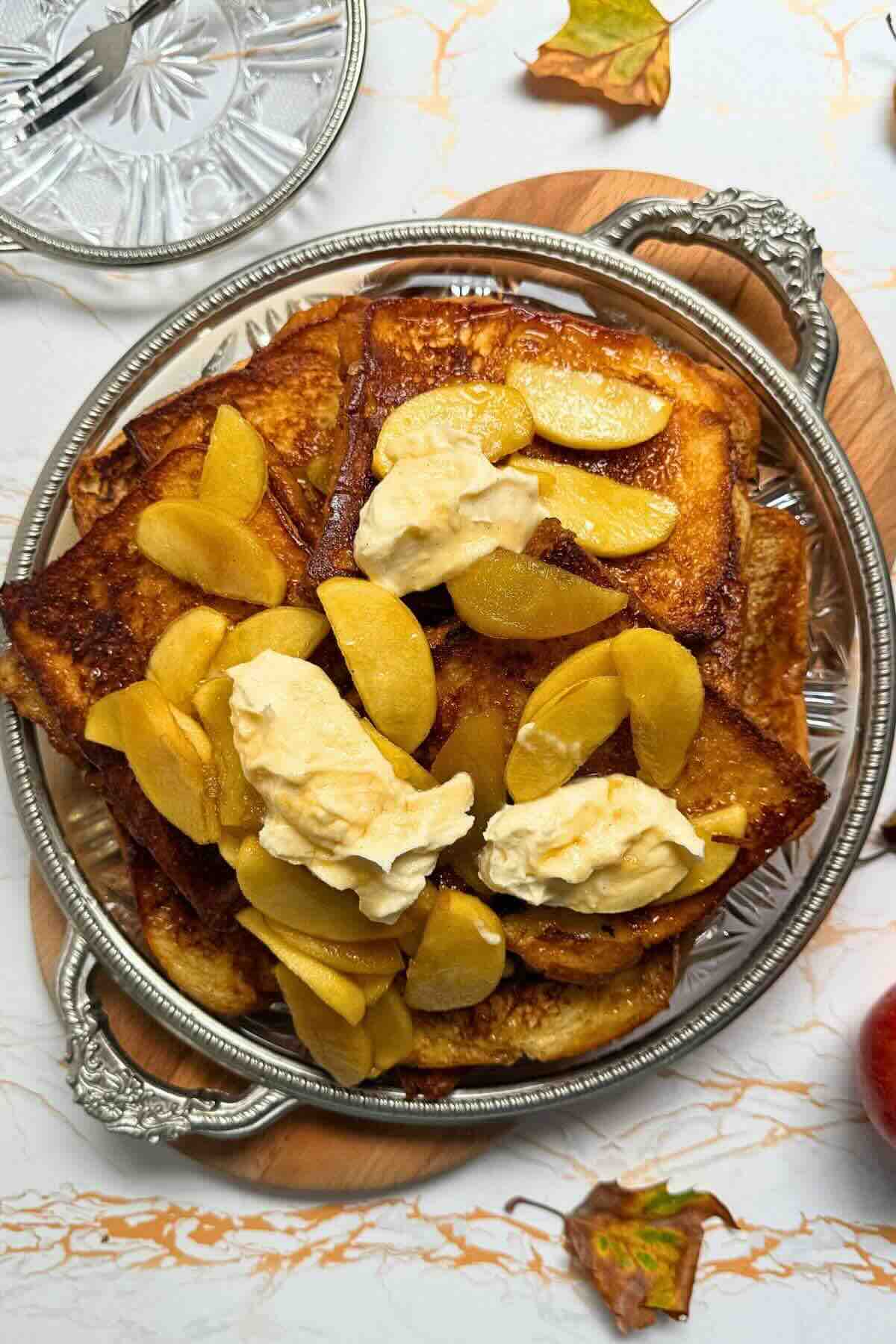 Golden brioche French toast topped with maple caramelized apples and a spoonful of whipped cream.