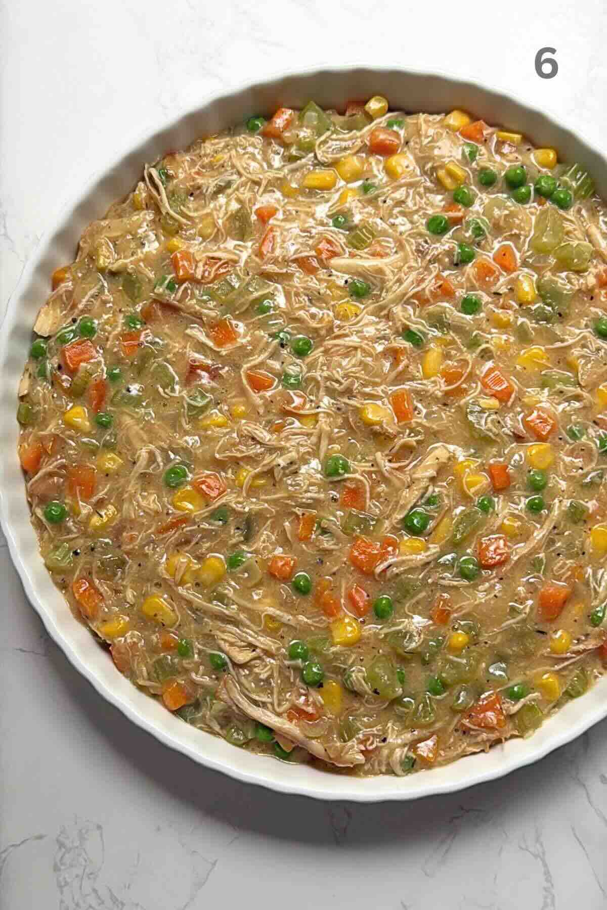 Creamy chicken and vegetable filling spread evenly in a ceramic baking dish.