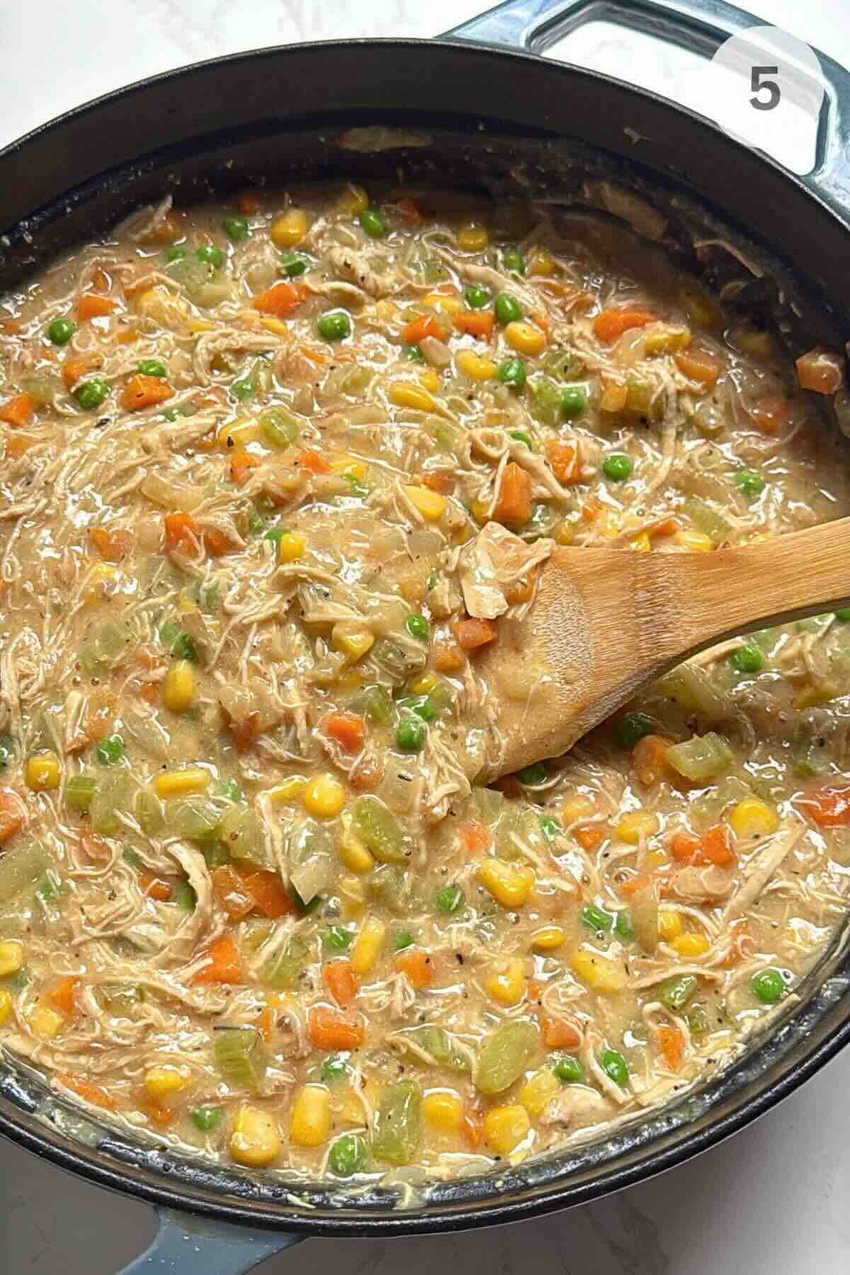 Shredded chicken stirred into a thickened creamy sauce with vegetables in a pan.