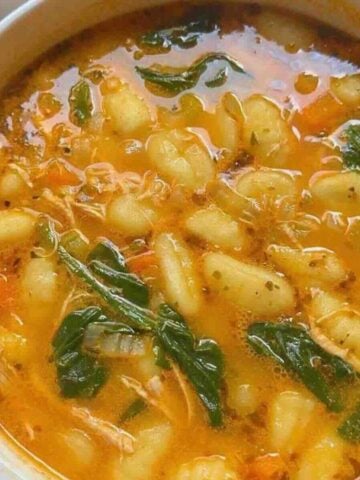 Pot of creamy chicken gnocchi vegetable soup with parsley garnish.