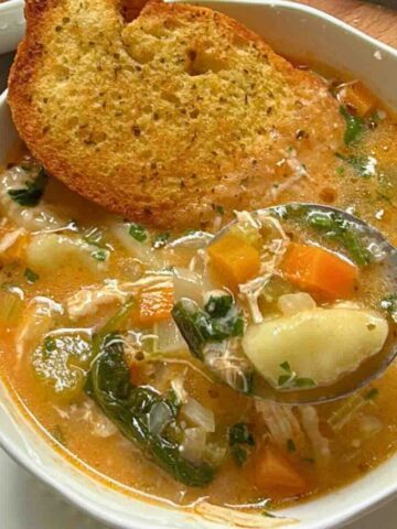Bowl of creamy chicken gnocchi vegetable soup with parsley garnish.