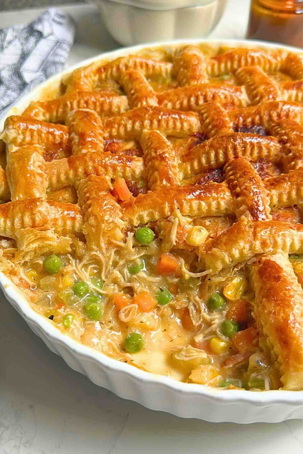 Braided puff pastry chicken pot pie in a ceramic dish, golden and crisp on top.