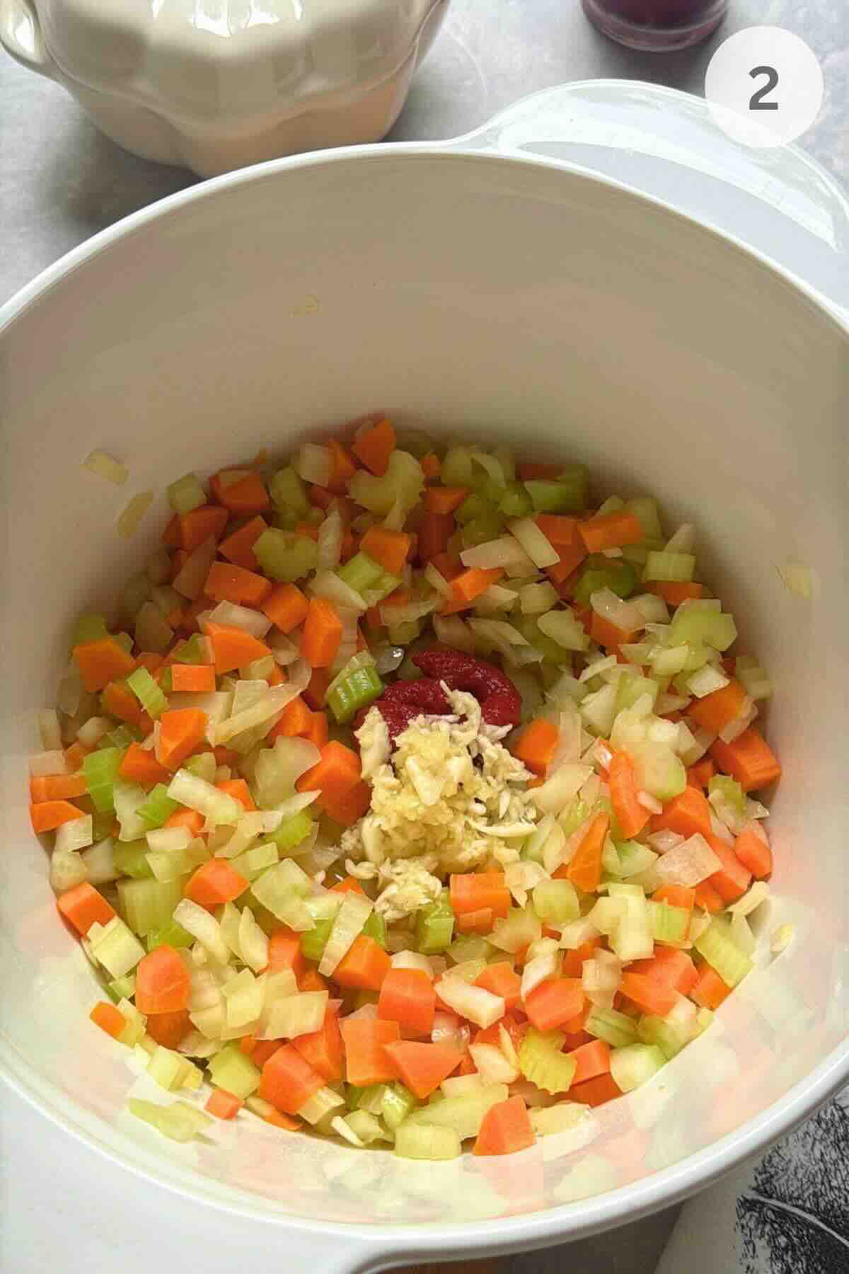 Onion, carrots, and celery softening in a pot with garlic and tomato paste.
