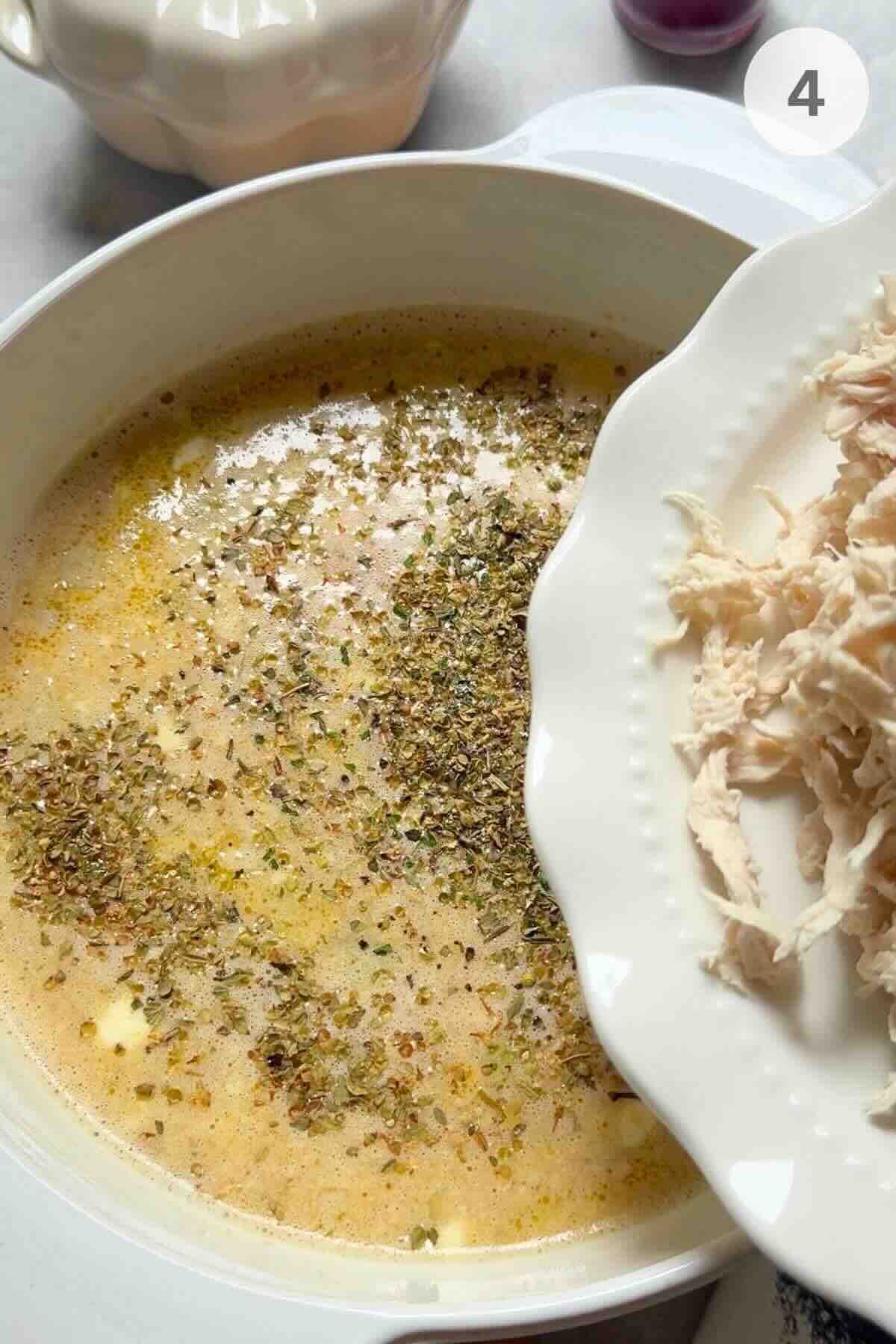 Shredded chicken being stirred into creamy vegetable broth in a soup pot.